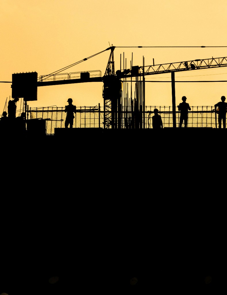 Silhouette of a construction crew and crane on a jobsite against a sunset sky