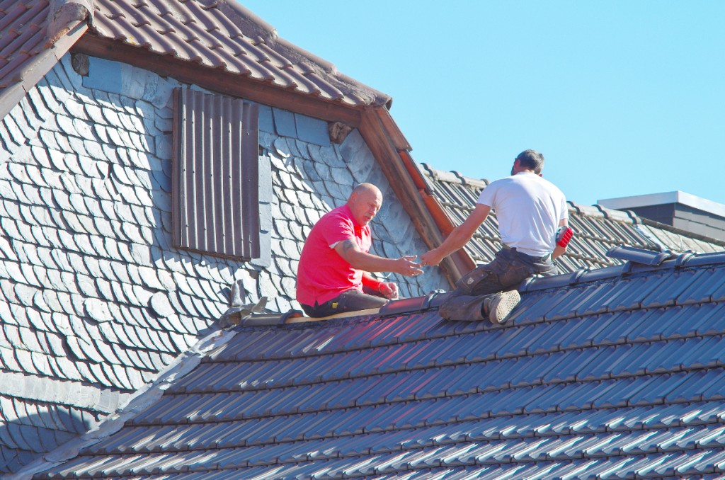 Roofers installing tiles on a residential roof during an in-progress job