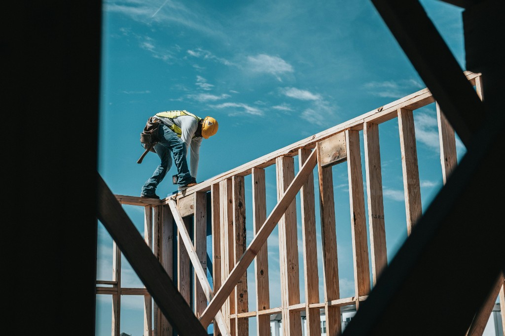 Framer working on a wood wall from below, against a clear sky